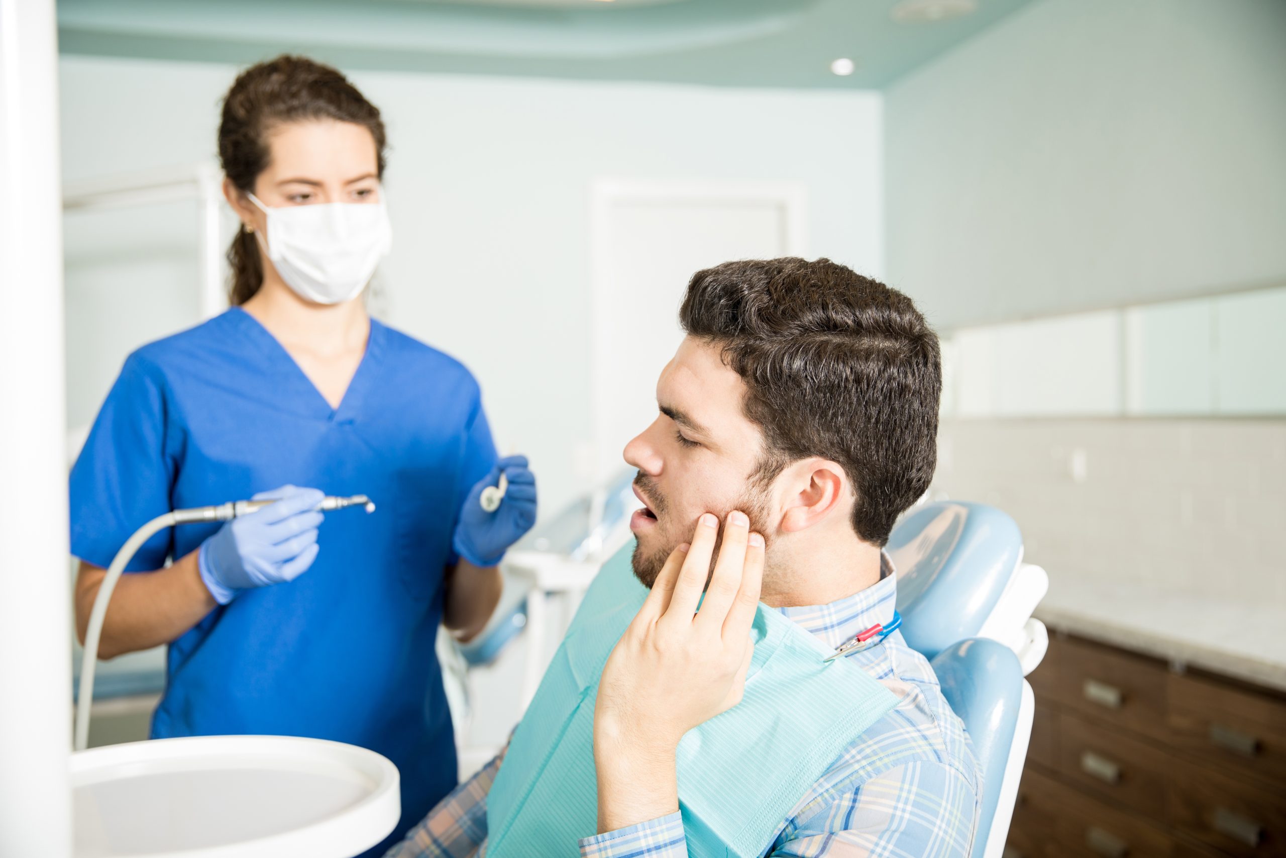 Man In Pain Looking At Dentist With Tools In Clinic